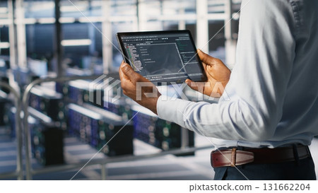 Data center admin checking code on tablet next to colleague reviewing AI visualizations in blurry background. IT experts use device to analyze neural networks outputs, ensuring stable gear operations 131662204