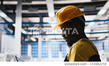Engineer using laptop to monitor solar panel plant assembly lines, troubleshooting photovoltaic equipment to ensure seamless production workflow. Automation for alternative energy. Camera A. Engineer using laptop to monitor solar panel plant assembly lines, troubleshooting photovoltaic equipment to ensure seamless production workflow. Automation for alternative energy. Camera A. 131662250