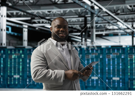 Portrait of cheerful technician in server hub checking recovery plan on tablet, monitoring energy consumption. Jolly data center staff member uses device, making sure sensors are functioning optimally Portrait of cheerful technician in server hub checking recovery plan on tablet, monitoring energy consumption. Jolly data center staff member uses device, making sure sensors are functioning optimally 131662291