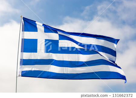 Against background of cloudy sky,white-blue flag of Greece flutters on flagpole 131662372