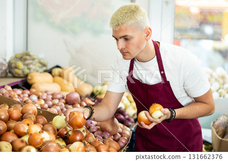 Guy shop seller puts onion goods on display case 131662376