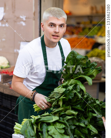 Grocery store employee places fresh spinach on display case at street store Grocery store employee places fresh spinach on display case at street store 131662380