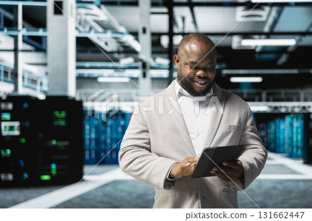 Happy data center engineer writing lines of code running on tablet, troubleshooting rackmounts. Cheerful IT professional using programming scripts on device in server room Happy data center engineer writing lines of code running on tablet, troubleshooting rackmounts. Cheerful IT professional using programming scripts on device in server room 131662447