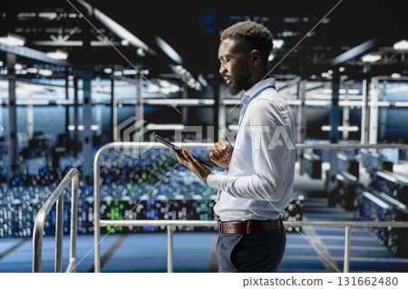 Young data center male employee on platform works on neural network software tasks. Confident african american engineer visualizing large language model architecture, technical support. Young data center male employee on platform works on neural network software tasks. Confident african american engineer visualizing large language model architecture, technical support. 131662480