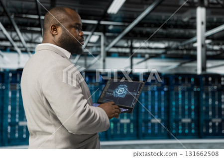 Data center system administrator using artificial intelligence computerized model on laptop. African american server room worker working with AI machine learning algorithms on device Data center system administrator using artificial intelligence computerized model on laptop. African american server room worker working with AI machine learning algorithms on device 131662508