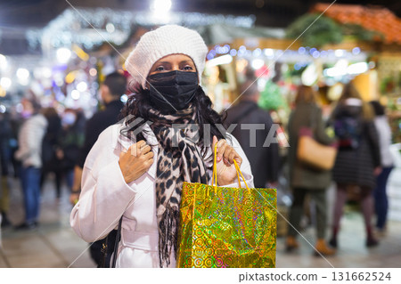 Woman in protective mask with shopping bags at Christmas fair Woman in protective mask with shopping bags at Christmas fair 131662524