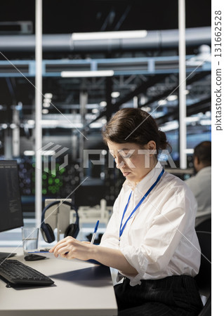 Server room worker holding clipboard, following procedures to evaluate system performance metrics. Woman in data center going over maintenance fixes list, running diagnostics on equipment. 131662528