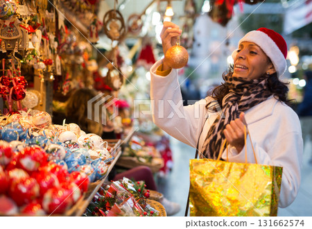 Hispanic woman in Santa hat choosing decorations at street Christmas fair Hispanic woman in Santa hat choosing decorations at street Christmas fair 131662574