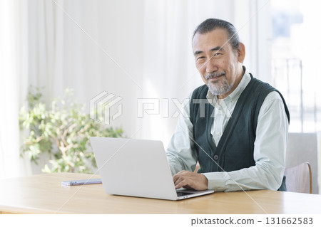 一位老人在筆記型電腦上工作,肖像看著相機,面帶微笑 一位老人在筆記型電腦上工作,肖像看著相機,面帶微笑 131662583