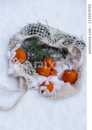 Ripe tangerines in reusable mesh bag with fir branch outside in snowy winter. Concept of sustainable Christmas celebration, responsibility and inclusivity. Oranges 131663050