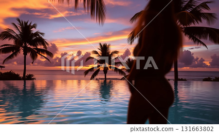 Silhouette of a beautiful woman relaxing in the pool in the setting light of the sun. The pool is surrounded by tropical trees. 131663802