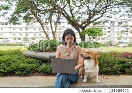 Remote Work and Pet Companionship. Young woman using laptop outdoors with her corgi dog. 131664495