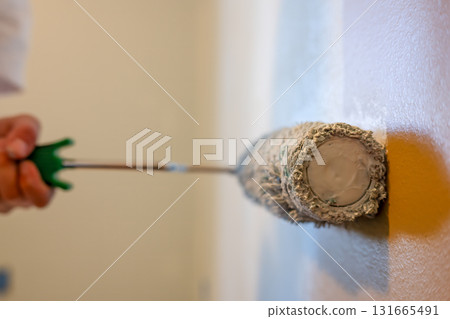 Rolling a fresh coat of paint on a wall using a paint roller in a bright room with soft lighting Rolling a fresh coat of paint on a wall using a paint roller in a bright room with soft lighting 131665491