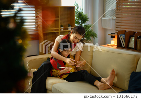 Mother and daughter spending quality time using tablet in warm holiday living room with festive decorations 131666172