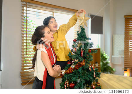 Happy mother lifting her daughter to place a star on top of the Christmas tree 131666173