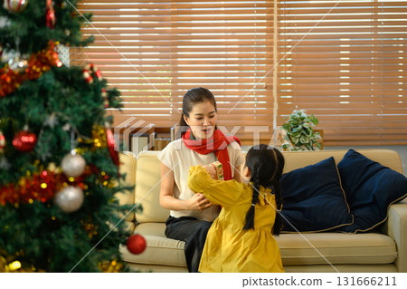 Cheerful mom receiving a present from her little girl near a decorated Christmas tree Cheerful mom receiving a present from her little girl near a decorated Christmas tree 131666211