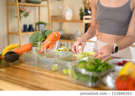 Fitness woman packing nutritious ingredients or weekly meal prep in a bright kitchen Fitness woman packing nutritious ingredients or weekly meal prep in a bright kitchen 131666263
