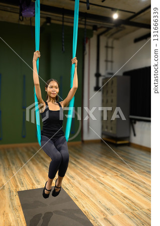 Young woman doing aerial yoga training, suspended in hammock for mindfulness, strength, and posture improvement 131666339