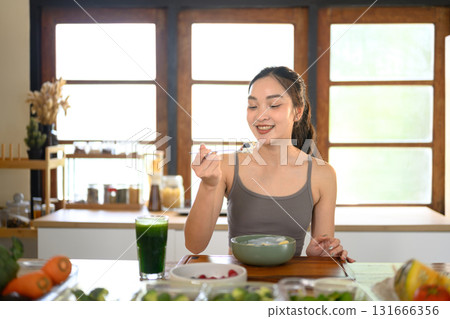 Active woman enjoying a yogurt bowl with fresh fruit, promoting self care and balanced nutrition at home 131666356