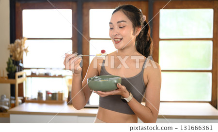 Young woman in sportswear eating a yogurt bowl with berries. Clean eating and healthy lifestyle concept. 131666361
