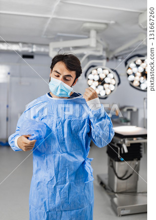 A surgeon prepares for an operation in a sterile operating room, adjusting his surgical mask. 131667260