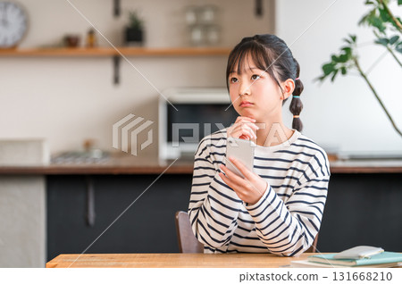 Elementary and junior high school girls using smartphones in the living room and dining room at home (troubled, thinking, worried, confused) Elementary and junior high school girls using smartphones in the living room and dining room at home (troubled, thinking, worried, confused) 131668210