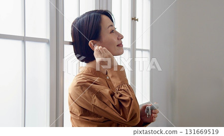 A woman listening to music or the radio by the window A woman listening to music or the radio by the window 131669519