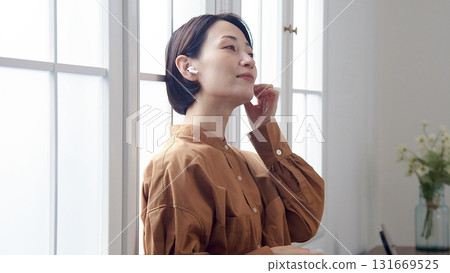 A woman listening to music or the radio by the window A woman listening to music or the radio by the window 131669525
