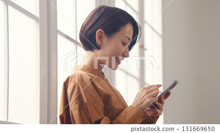A woman using a phone by the window A woman using a phone by the window 131669650
