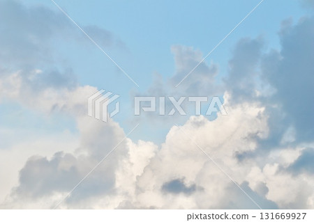 A mix of dark grey storm clouds and bright white cumulus formations against a pale blue sky, showing the transition of weather and dramatic atmospheric contrast. 131669927