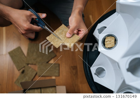 Close-up top view of gardener hands cutting rockwool with scissors, preparing hydroponic media for seed starting, highlighting precision in indoor cultivation techniques. Concept of home gardening. 131670149