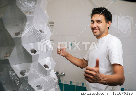 Cheerful gardener male unpacking vertical hydroponic gardening system tower in bathroom, preparing for installation and setting up, showing thumbs up gesture, smiling looking at camera. Cheerful gardener male unpacking vertical hydroponic gardening system tower in bathroom, preparing for installation and setting up, showing thumbs up gesture, smiling looking at camera. 131670189