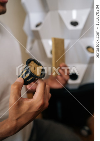 Vertical cropped shot of unrecognizable gardener holding net pot and rockwool cube, preparing for seed starting in hydroponic tower garden, promoting sustainable and efficient indoor farming at home. 131670204