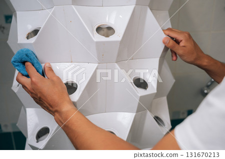 Close-up of unrecognizable gardener male cleaning white hydroponic system with rag, ensuring optimal conditions for plant growth in modern indoor garden setup, promoting healthy cultivation. 131670213