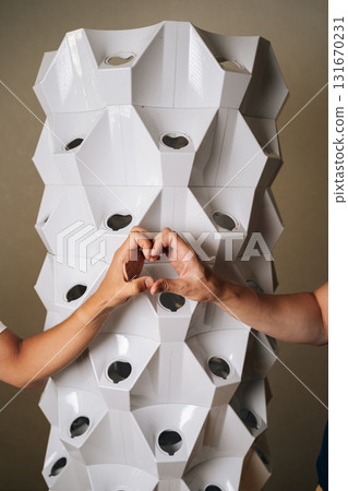 Vertical cropped shot of unrecognizable gardeners making heart shape with hands by vertical hydroponic tower garden, showcasing love and care for innovative and sustainable agriculture. Vertical cropped shot of unrecognizable gardeners making heart shape with hands by vertical hydroponic tower garden, showcasing love and care for innovative and sustainable agriculture. 131670231