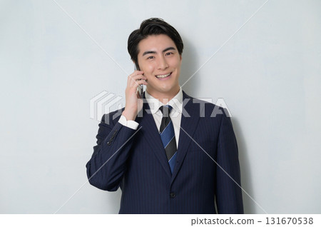 A man in a suit talking on a phone against a white background A man in a suit talking on a phone against a white background 131670538