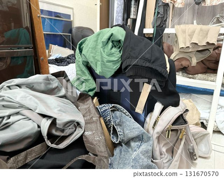 A woman's messy room - green clothes, carry-on bags, etc. 131670570