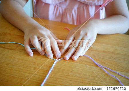 A child in pink clothes knitting a friendship bracelet A child in pink clothes knitting a friendship bracelet 131670710