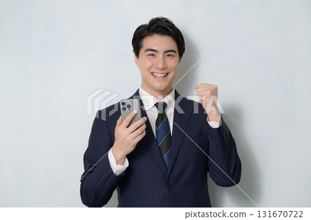 A man in a suit holding a smartphone and making a fist pump A man in a suit holding a smartphone and making a fist pump 131670722