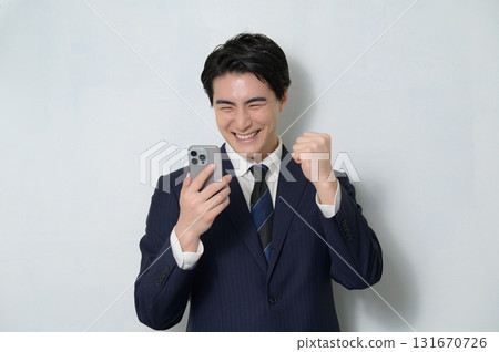 一名西裝革履的男子手持智慧型手機,揮拳 一名西裝革履的男子手持智慧型手機,揮拳 131670726
