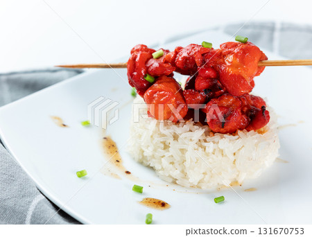 Seasoned red chicken skewers served on a small mound of white steamed sticky rice on a square white plate. Asian or fusion cuisine. 131670753