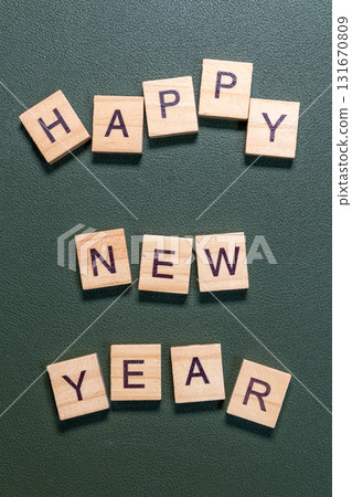 Wooden letter tiles spelling Happy New Year arranged neatly on a textured green background 131670809