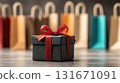 A black gift box with a red bow against a background of colorful paper shopping bags. Concept for holiday sales, gift shopping, online shopping, Black Friday, and Cyber Monday. 131671091