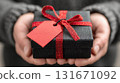 A close-up of a person's hands holding a black gift box with a red bow and an empty tag for text. Holiday seasonal sales, gift shopping 131671092