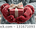 A close-up of a person's hands in red winter gloves holding a black gift box with a red bow outside during a winter snowfall. Holiday seasonal sales, gift shopping 131671093
