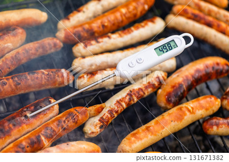 Raw sausages on barbecue with digital meat thermometer showing unsafe low temperature 131671382
