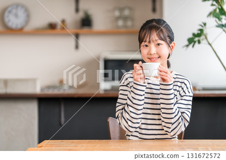 小學和中學的女孩們在家裡的客廳喝熱飲 小學和中學的女孩們在家裡的客廳喝熱飲 131672572