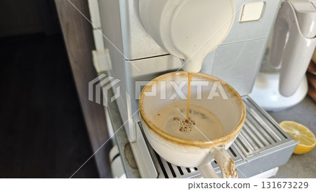 Fresh espresso pours into a ceramic cup from a coffee machine in a cozy kitchen setting, capturing the aroma of morning coffee. 131673229