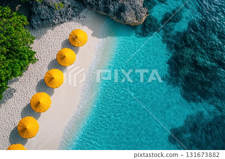 Vibrant yellow umbrellas line a sandy beach next to clear blue waters on a sunny day in a tropical paradise 131673882