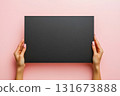 Blank black canvas held by hands against a soft pink background showcases potential for creativity in art and design projects 131673888